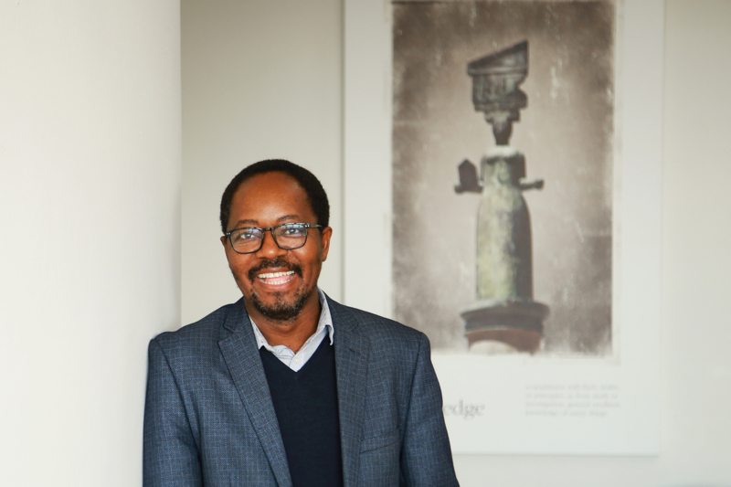 The Dean leans against a column, smiling at the camera